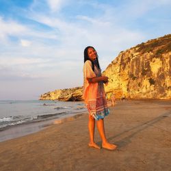 Side view portrait of smiling woman standing at beach against sky