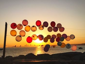 Multi colored balloons on beach against sky during sunset