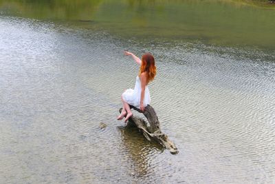 Full length of woman pointing while sitting on wood over lake