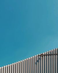 Low angle view of cctv camera on a wall against clear blue sky