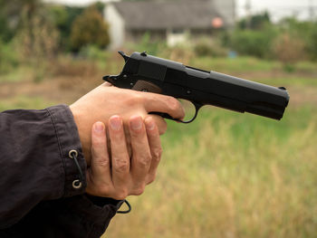 Cropped hands of thief holding gun on field