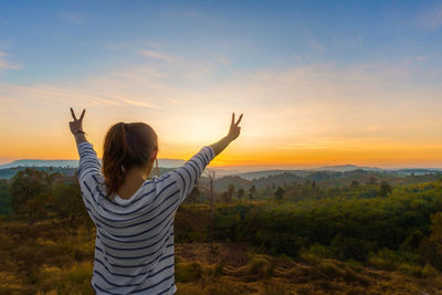 Rear view of woman gesturing while standing on land against sky during sunset