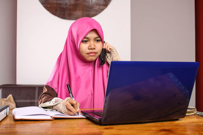 Young woman talking on telephone while using laptop at home