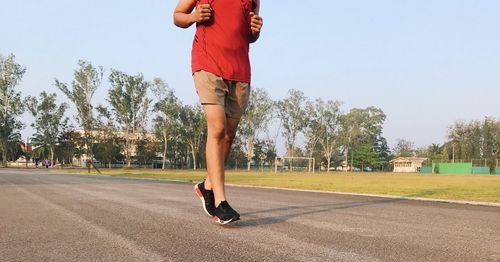 Low section of man running on street against sky