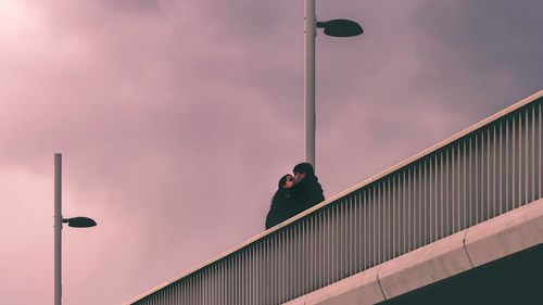 Low angle view of man standing on street light against sky