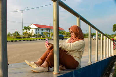 Woman sitting on railing against sky