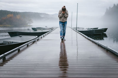 Young woman looking down while walking across wet dock in the fog