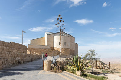 Rear view of man walking by building against sky