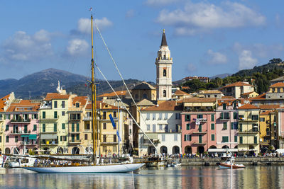 Sailboats in river by buildings in city against sky