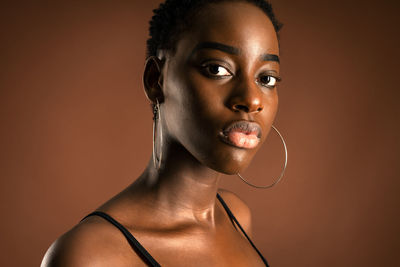 Slender black woman with short hair standing against brown background looking at camera