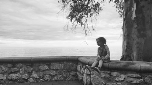 Boy sitting by sea against sky