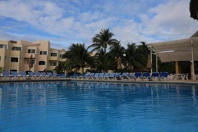 Swimming pool by palm trees against sky