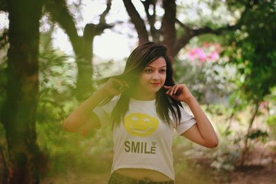 Portrait of young woman standing against trees