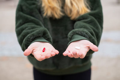 Midsection of woman with red and white pill standing on road