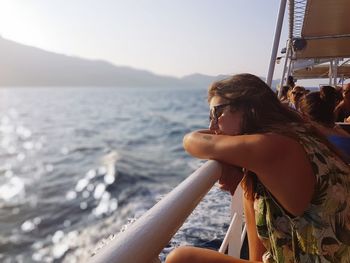 Woman with eyes closed relaxing on railing of nautical vessel at sea