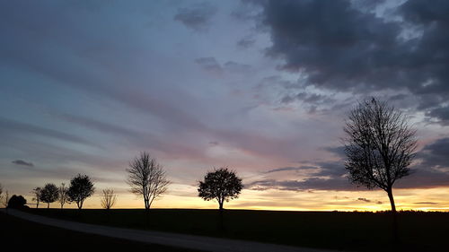 Silhouette trees on landscape against dramatic sky