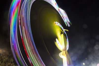 Low angle view of illuminated ferris wheel spinning at night