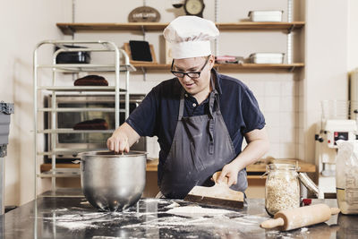 Young man making dough at kitchen counter