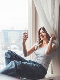 Woman with curly hair poses for selfie on windowsill. woman makes self-portrait on smartphone.