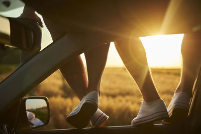 Low section of couple on car roof during sunset