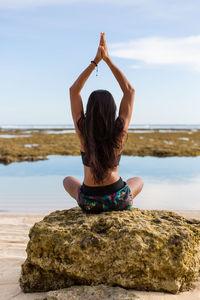 Rear view of young woman doing yoga on beach