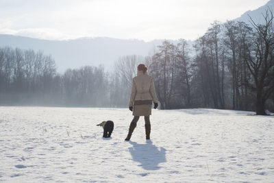 Rear view of woman with dog standing on snow covered field