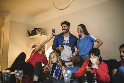 Male and female using smart phone while watching soccer match at home