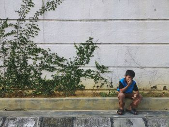 Full length of boy sitting on retaining wall against wall