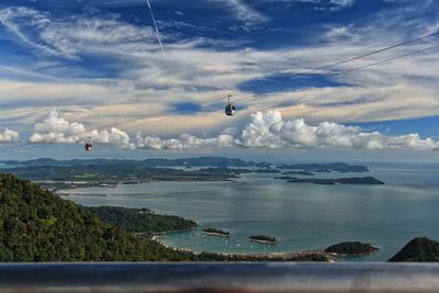 Overhead cable car over sea against cloudy sky