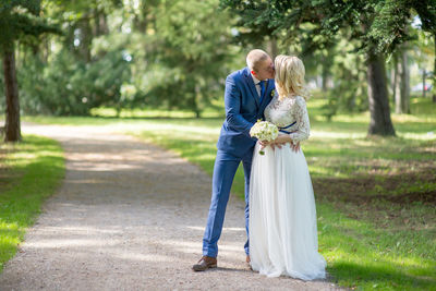 Full length of bride and bridegroom kissing on footpath at park