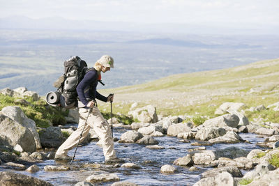 Side view of man walking on stones in stream