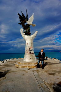 Full length of man standing by statue against sky