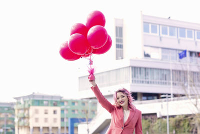 Portrait of woman with pink balloons standing against building in city