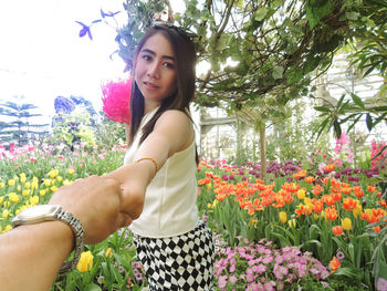 Cropped image of boyfriend holding beautiful girlfriend hand by flowering plants