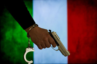 Cropped hand of male criminal holding gun against italian flag