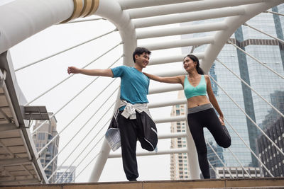 Smiling friends exercising on bridge in city