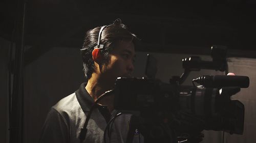 Man with television camera standing against black background