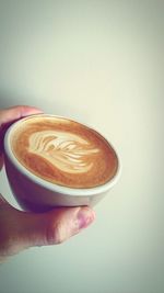 Close-up of hand holding coffee cup over white background