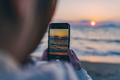 Man photographing sea through smart phone during sunset