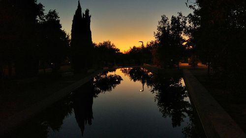 Reflection of silhouette trees in lake against sky at sunset