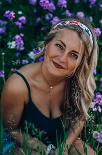 Portrait of smiling young woman sitting amidst flowering plants