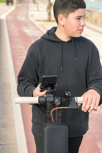 Young teenager with a sideways glance riding an electric scooter and using a smartphone application
