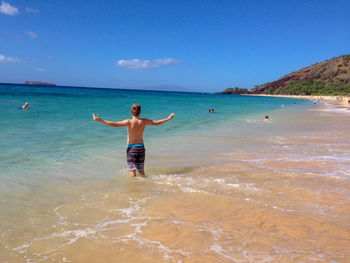 Rear view of shirtless man standing in sea against sky