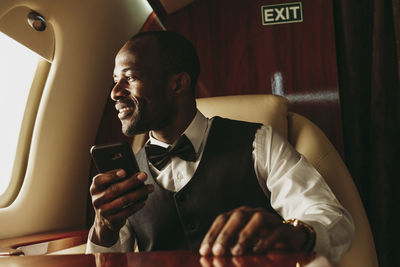 Male entrepreneur holding smart phone while looking out of window in airplane