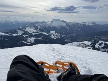 Low section of person on snowcapped mountain against sky