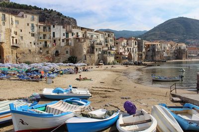 Boats moored on beach by buildings against sky