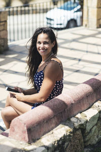 Portrait of smiling woman using mobile phone while sitting on bench