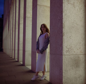 Portrait of woman walking on footpath by column