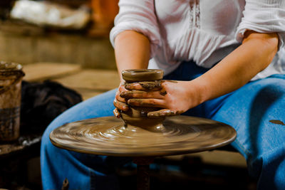 Midsection of woman molding shape on pottery wheel