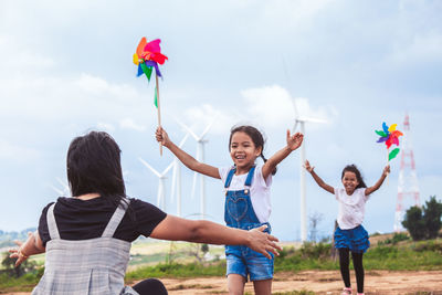 Mother and daughters playing with pinwheel toys on land with windmills in background